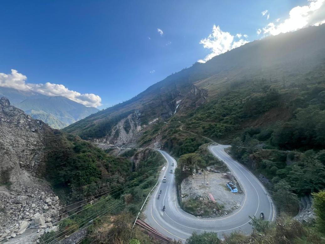 Hairpin bends of a mountain road below steep, debris-covered slopes in the Nepal Himalaya
